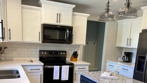 A modern kitchen with white cabinetry, a black stove, and a granite island. - Raffaele`s Retreat - Tri-Level, Modern, Near Beach (South Haven)