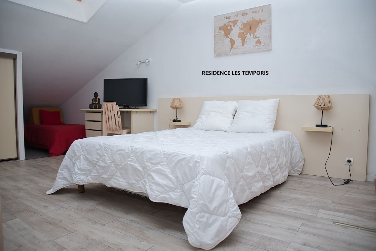 A bedroom with a bed, a desk, a chair, a television, and a world map on the wall.