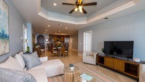 A spacious living room with a large TV, a ceiling fan, and a dining area in the background. - Cozumel-Beautiful 2 bedroom ocean view condo (San Miguel de Cozumel)