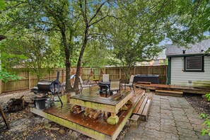 A backyard with a barbecue grill, wooden deck, and a covered seating area.