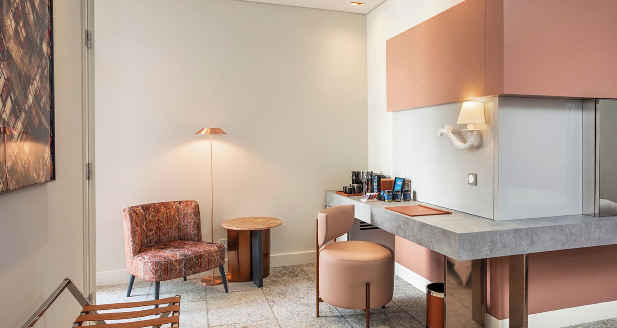 A hotel room with a seating area, a small round table, a sofa, a coffee station, and a large mirror.