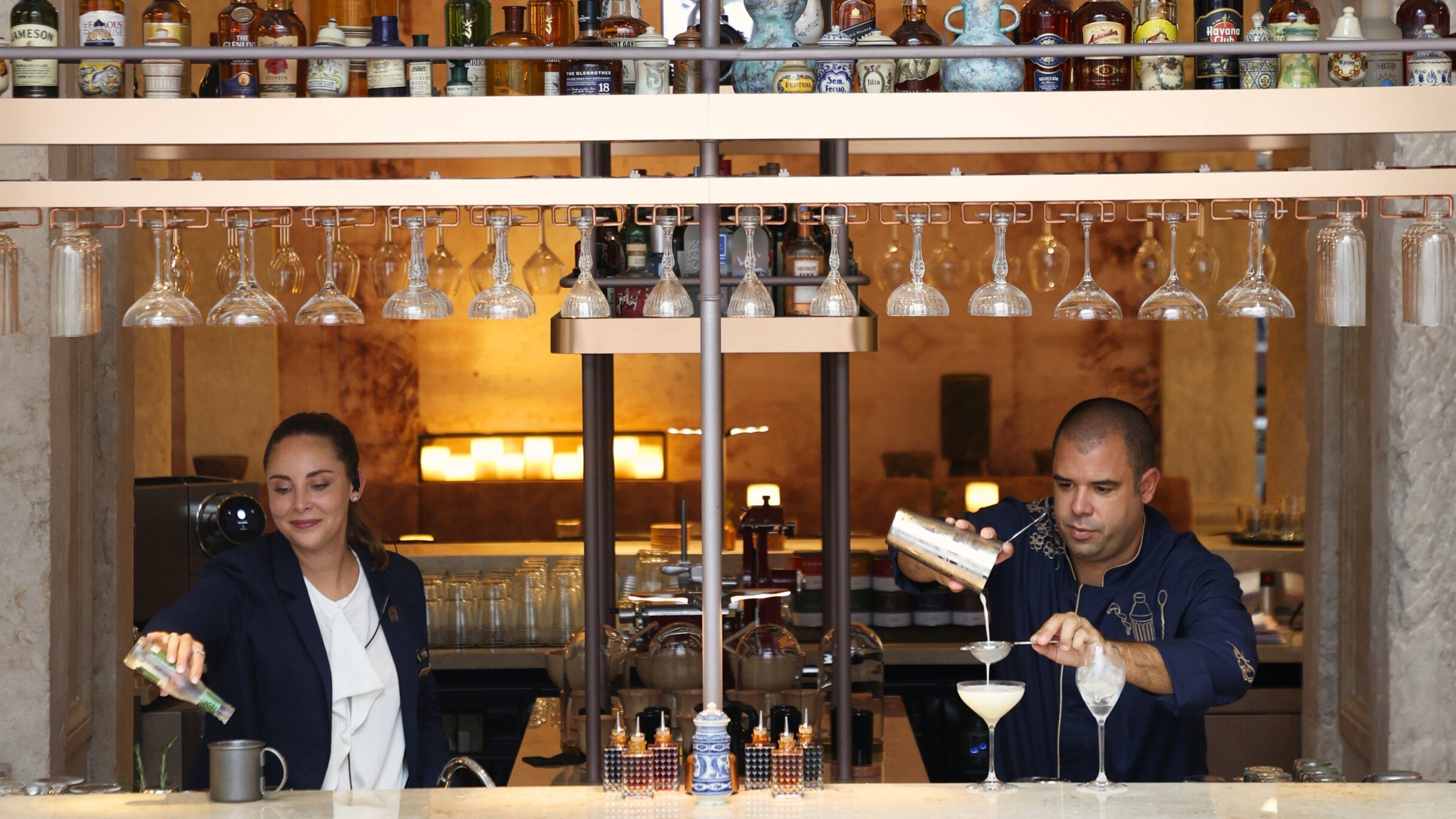 Zona de bar con estantes llenos de botellas de licor y un barman preparando una bebida.