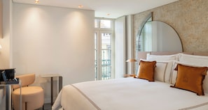 A hotel room with a large bed, a desk with a chair, a mirror, and a balcony view.