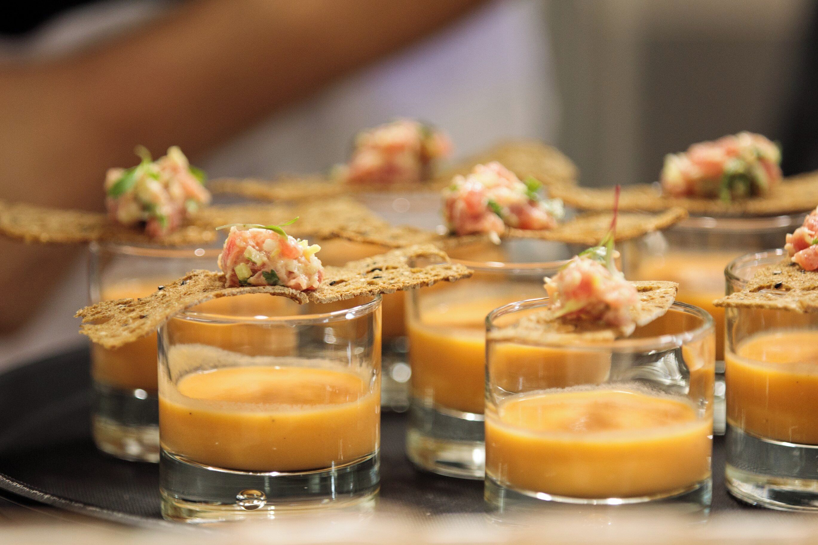 A series of small glasses containing a creamy dessert, each topped with a piece of bread and a small dollop of a pinkish topping.