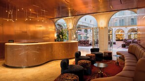 A modern lobby with a curved reception desk, seating area with ottomans, and large arched windows offering views of the street. - Convent Square Lisbon, Vignette Collection by IHG (Lisbon)