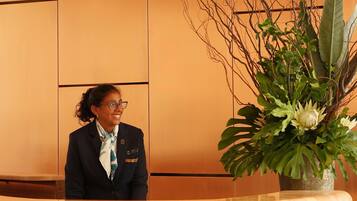 A reception desk with a receptionist, a large potted plant with green foliage, and a marble counter.