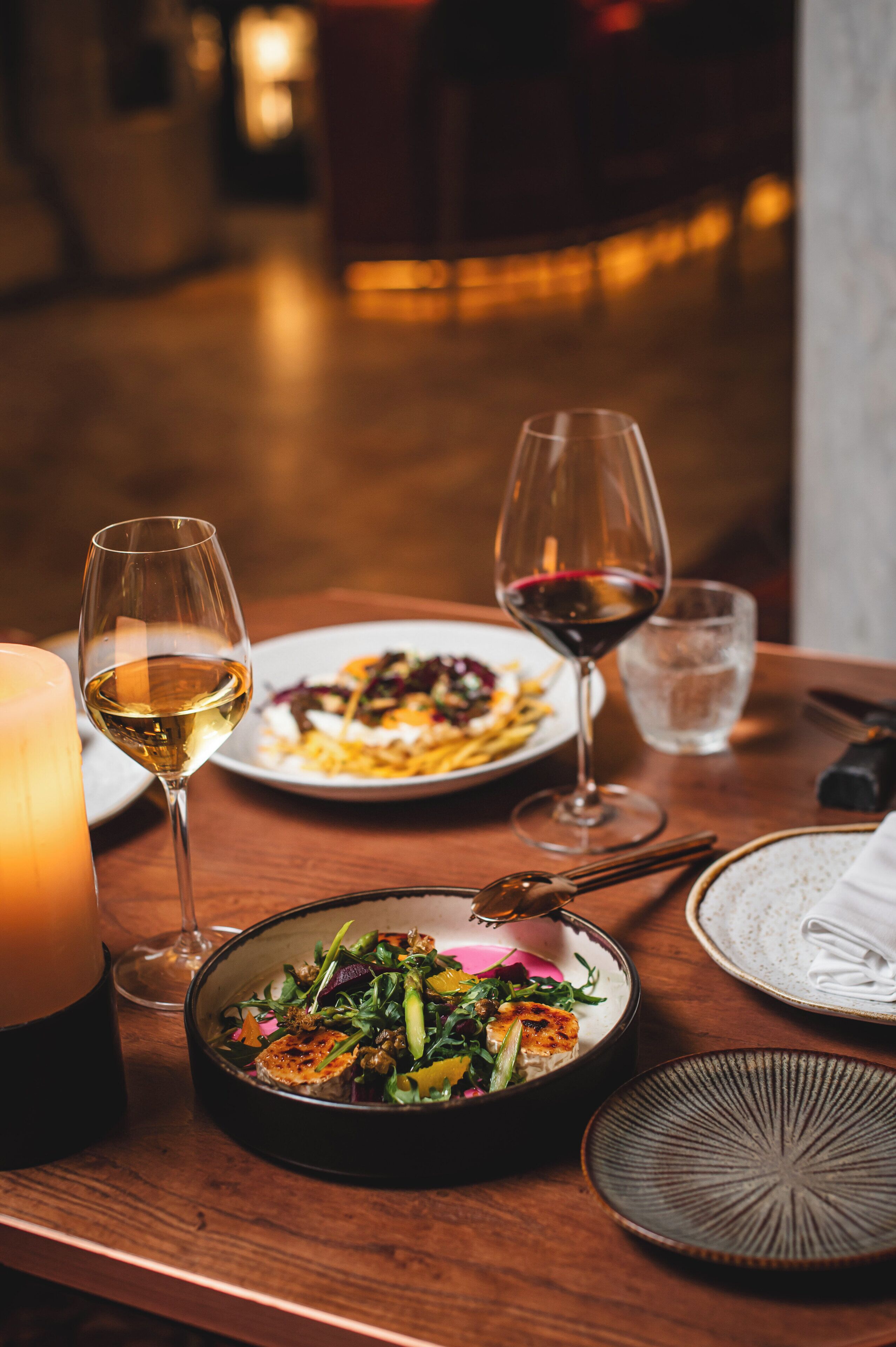 Une table à manger avec des assiettes remplies de nourriture, des verres de vin et une bougie.