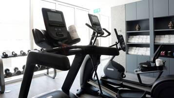 A gym with two treadmills, a weight rack, and neatly folded towels on shelves.
