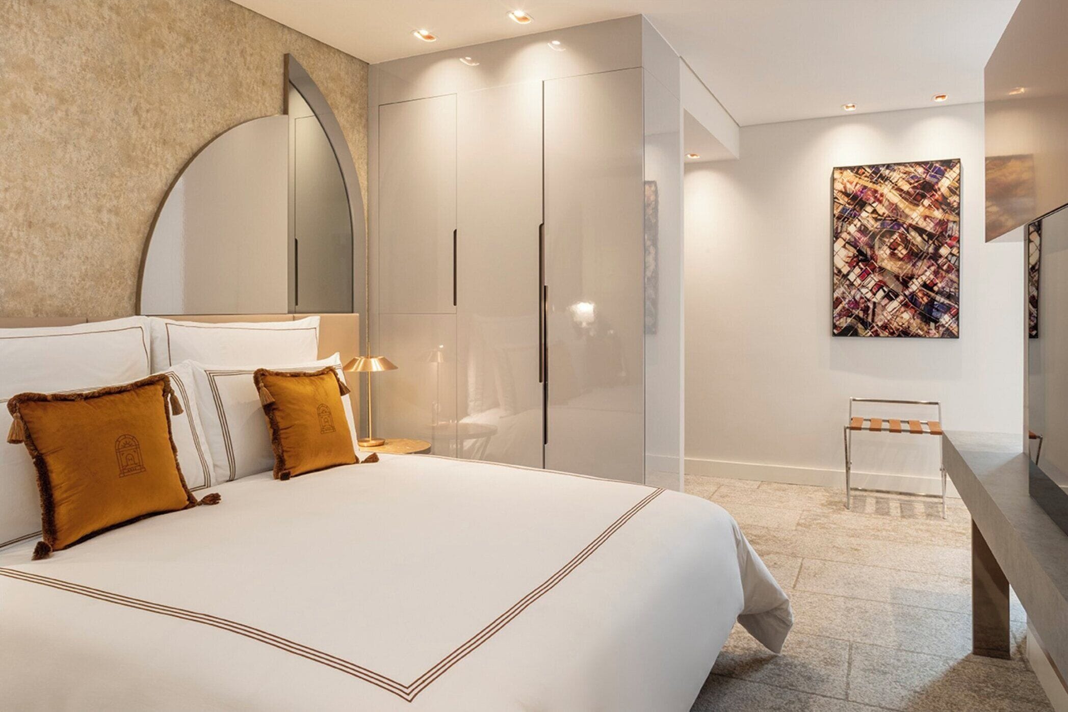 A modern hotel room with a large bed, a mirror, a wardrobe, a TV, and a painting on the wall.