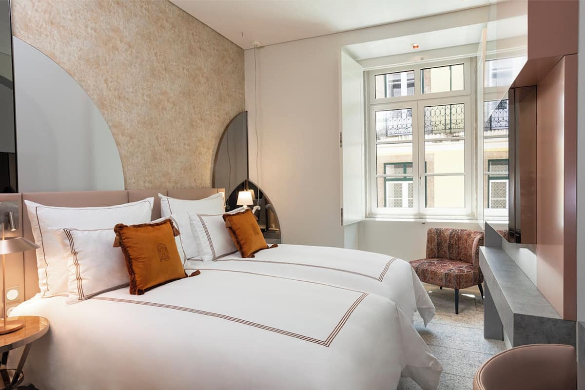 A hotel room with a large bed, a chair, a desk, and a window with a view of buildings.