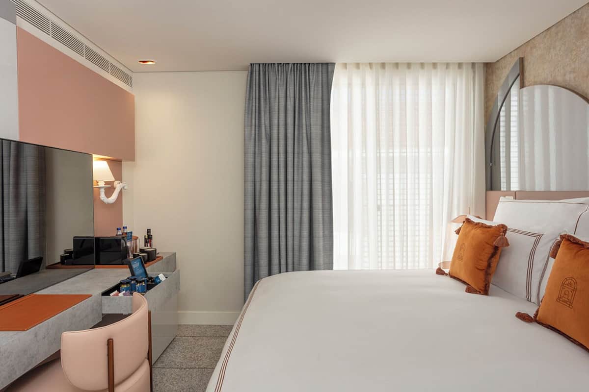 A hotel room with a bed, a desk with a computer, a television, and a window with curtains.