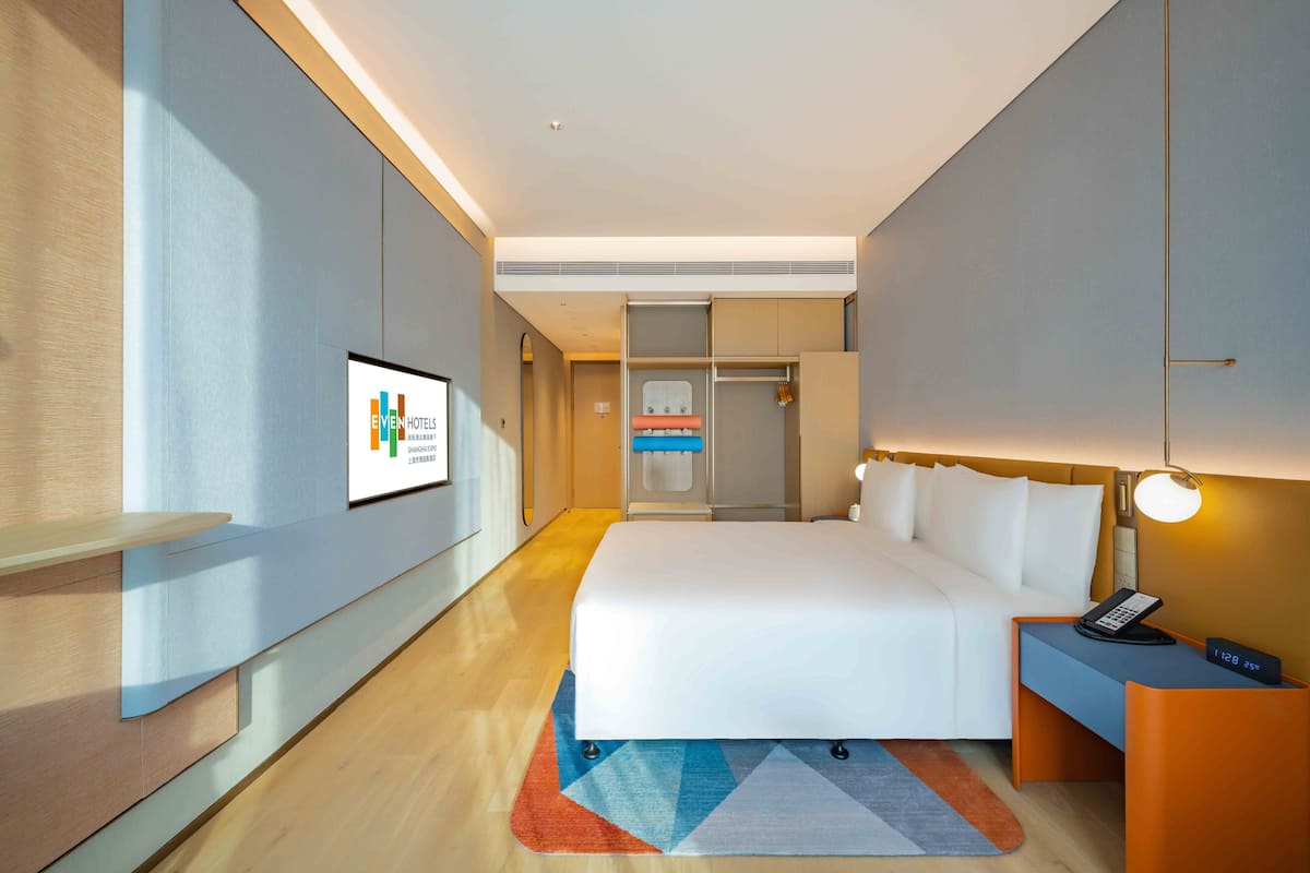 A modern hotel room with a large bed, bedside table with a phone, and a wall-mounted TV.
