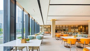 Een moderne eetruimte met grote ramen, meerdere tafels en stoelen.