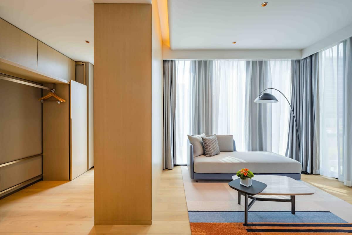 A modern hotel room with a large bed, a sofa, a coffee table, and a wardrobe.