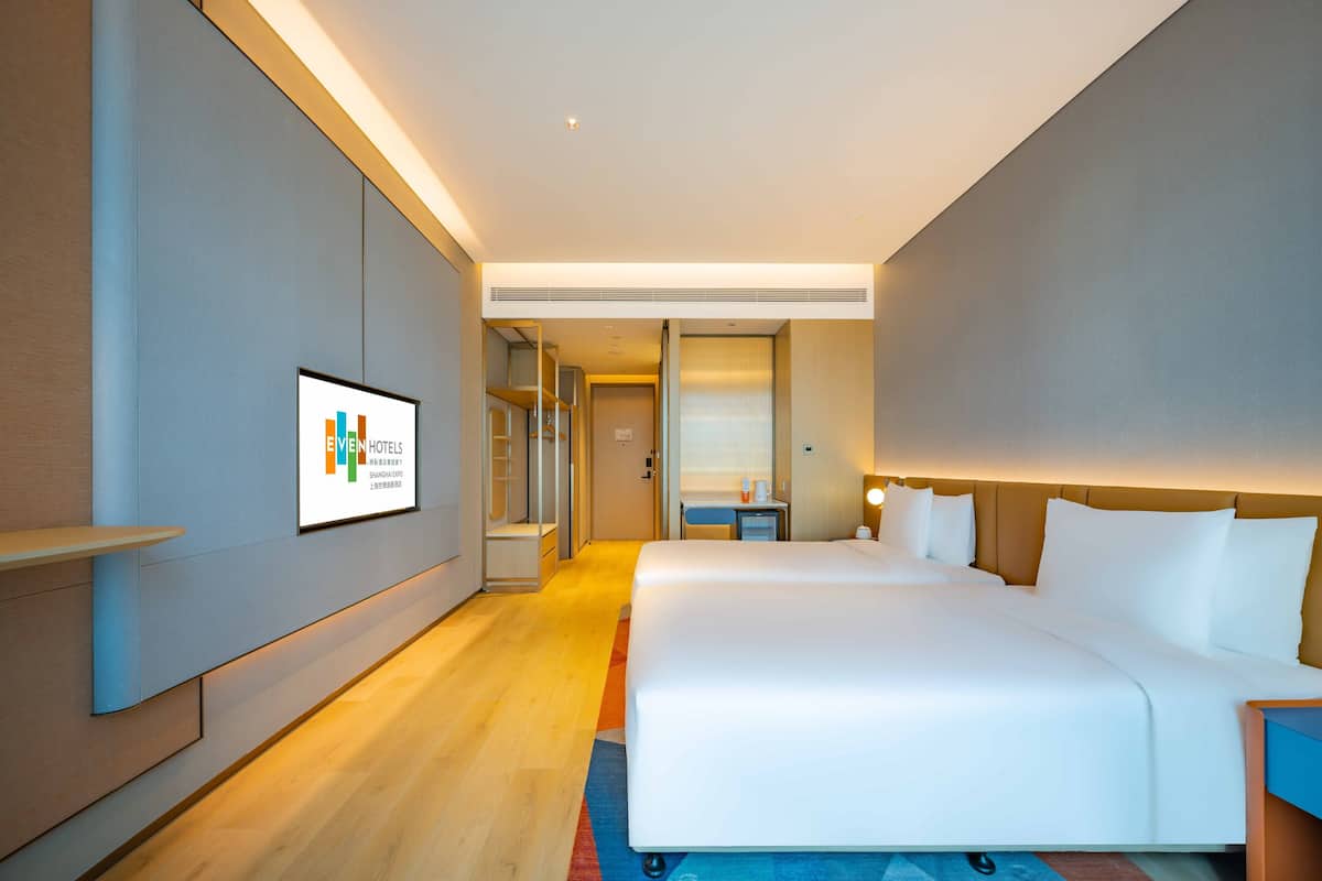 A modern hotel room with a large bed, a bedside table, a nightstand, and a wall-mounted TV.