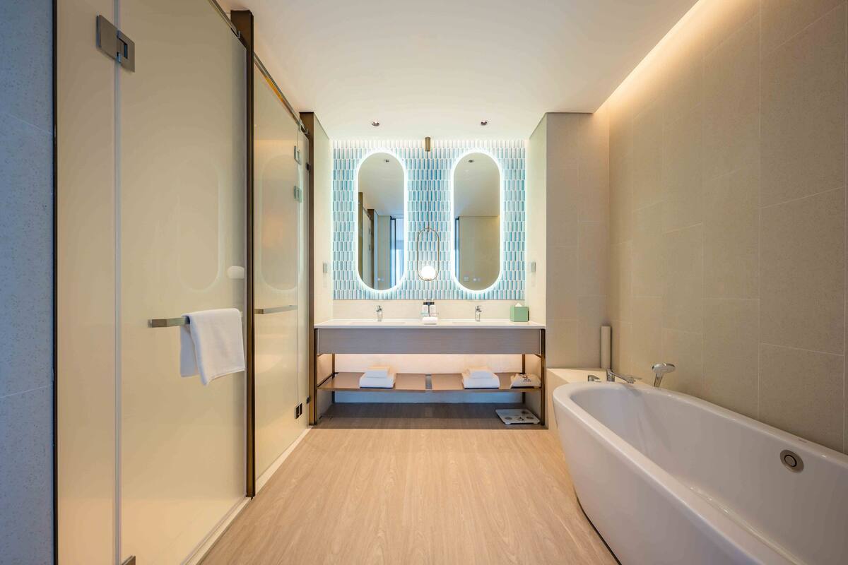 Un baño moderno con cabina de ducha de vidrio, una bañera independiente y un tocador con dos lavamanos y un espejo grande.