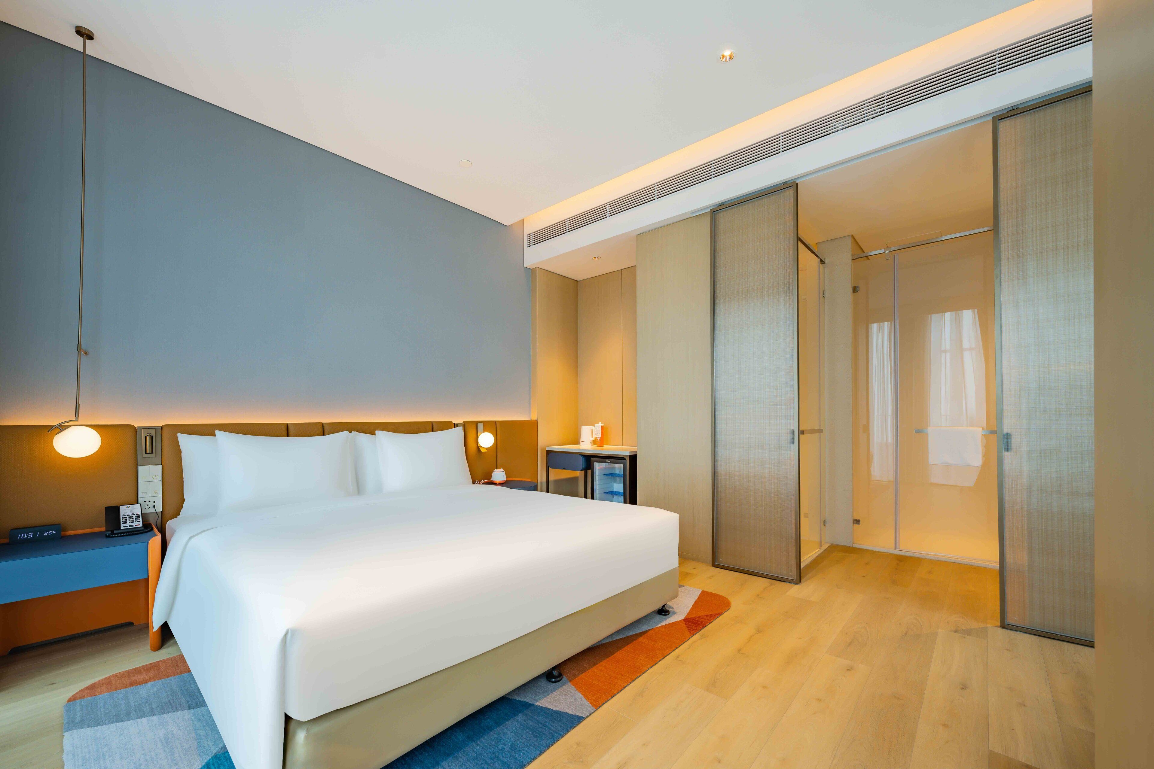 A modern hotel room with a large bed, bedside tables, a desk, and a walk-in closet.