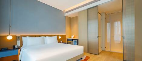 A modern hotel room with a large bed, bedside tables, a desk, and a walk-in closet.