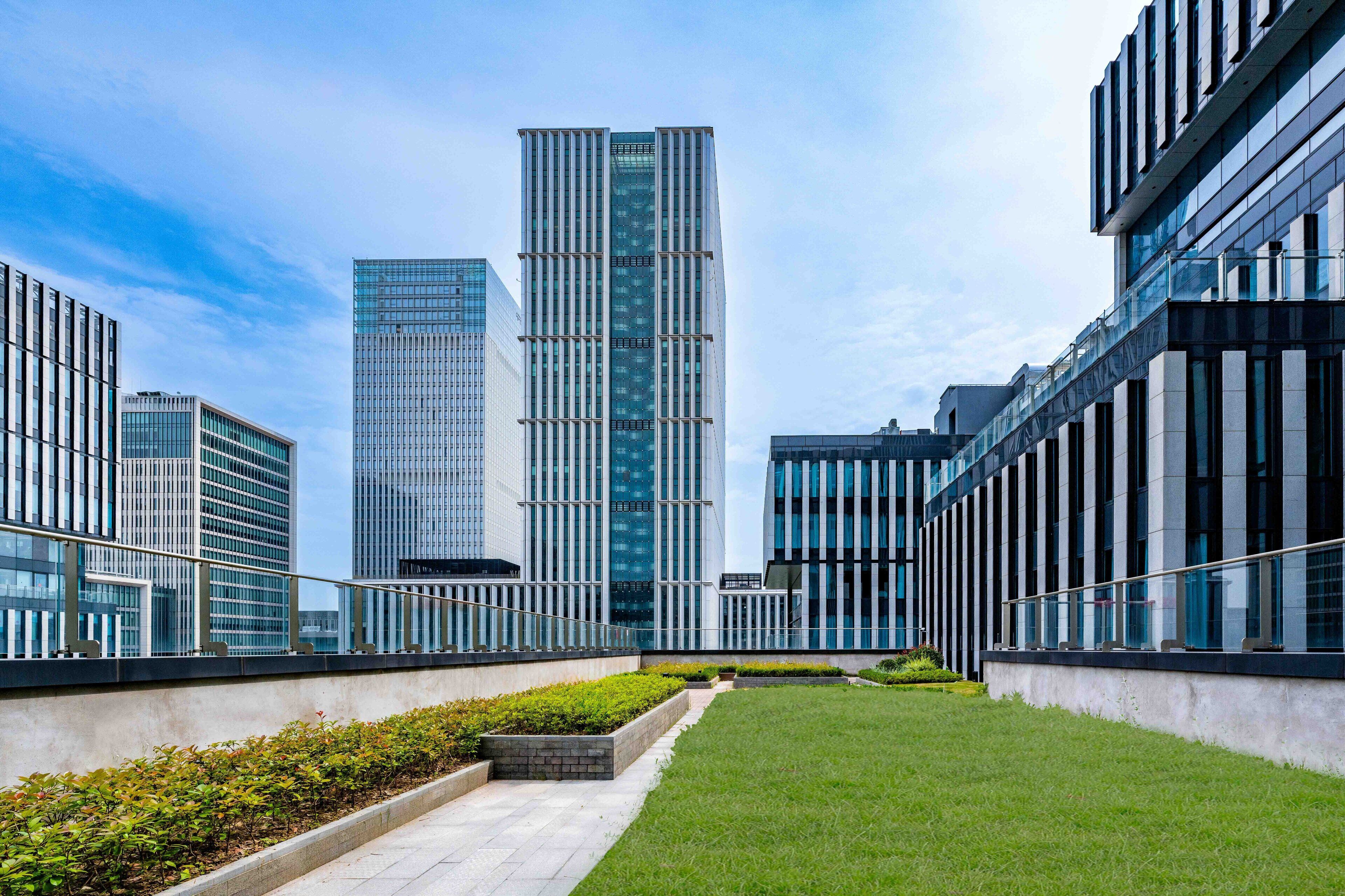 Un complex modern d'edificis amb diverses torres alts i una torre de vidre central, juntament amb una zona d'altes gespa ben cuidada.