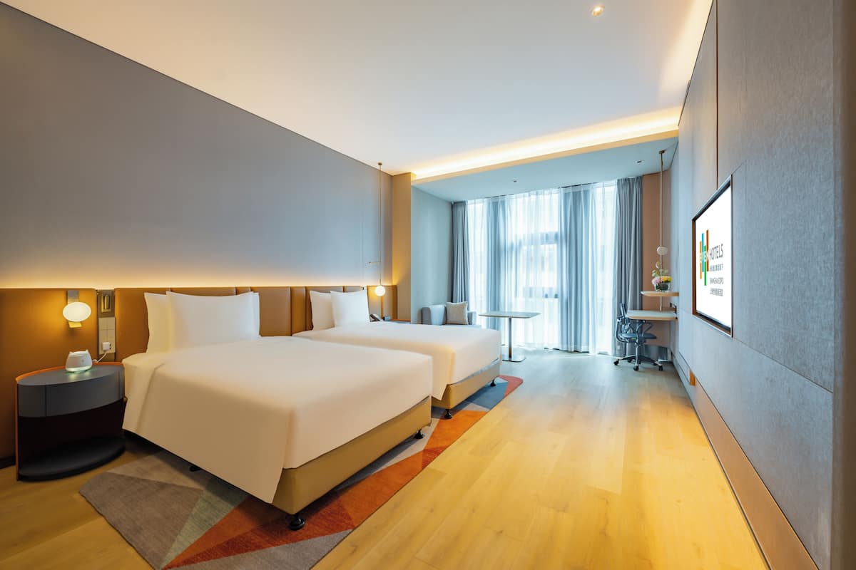 A hotel room with two beds, a desk, a chair, and a small table.