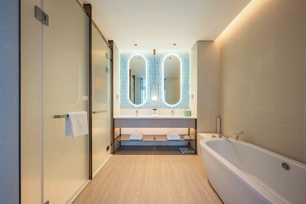 A modern bathroom with a glass shower enclosure, a freestanding bathtub, and a vanity with two sinks and a large mirror.