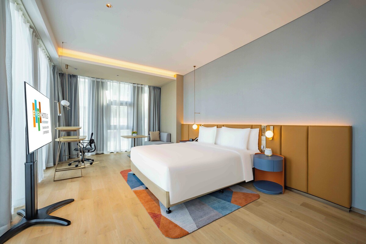 A modern hotel room with a large bed, a desk, and a TV.