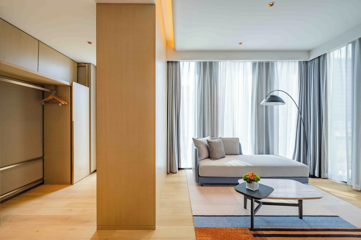 A modern hotel room with a large bed, a sofa, a coffee table, and a wardrobe.