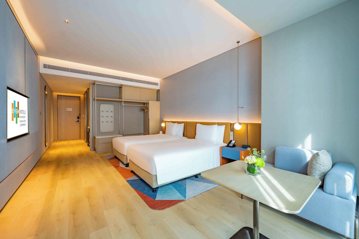 A modern hotel room with a large bed, a sofa, a small table, and a desk.