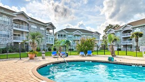 A swimming pool with a brick deck, surrounded by lounge chairs and potted plants. - Golf, Swim & Unwind at Bright Myrtle Beach Condo! (Myrtle Beach)