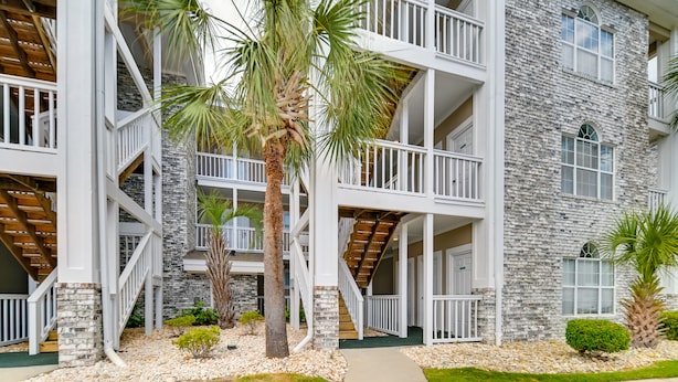 A multi-story building with a stone facade, balconies, and a palm tree in the foreground. - Golf, Swim & Unwind at Bright Myrtle Beach Condo! (Myrtle Beach)