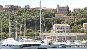 Un port de plaisance où sont amarrés de nombreux yachts, entouré de bâtiments et d’une colline sur laquelle se dresse une structure ressemblant à un château.
