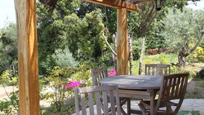 Une pergola en bois installée à l’extérieur, avec une table et des chaises, entourée de verdure et de fleurs.