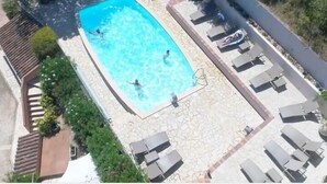 Une piscine rectangulaire, bordée d’une terrasse carrelée, entourée de chaises longues et d’un chemin en pierre.