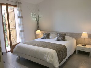 Une chambre à coucher comprenant un lit, deux lampes de chevet, une table de nuit, une plante décorative et une porte-fenêtre coulissante donnant sur un espace extérieur.