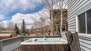 Un bain à remous sur une terrasse, avec une clôture en bois, un banc en bois et une vue sur une maison et des arbres.