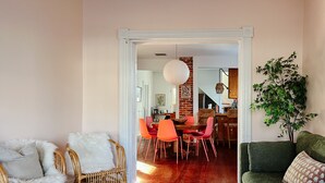 Een woonkamer met een eethoek, met rieten stoelen, een groene bank en een witte salontafel.