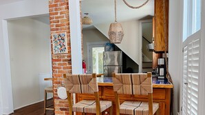 Een eetgedeelte met een bakstenen muur, houten stoelen, een tafel en een hangende lamp.