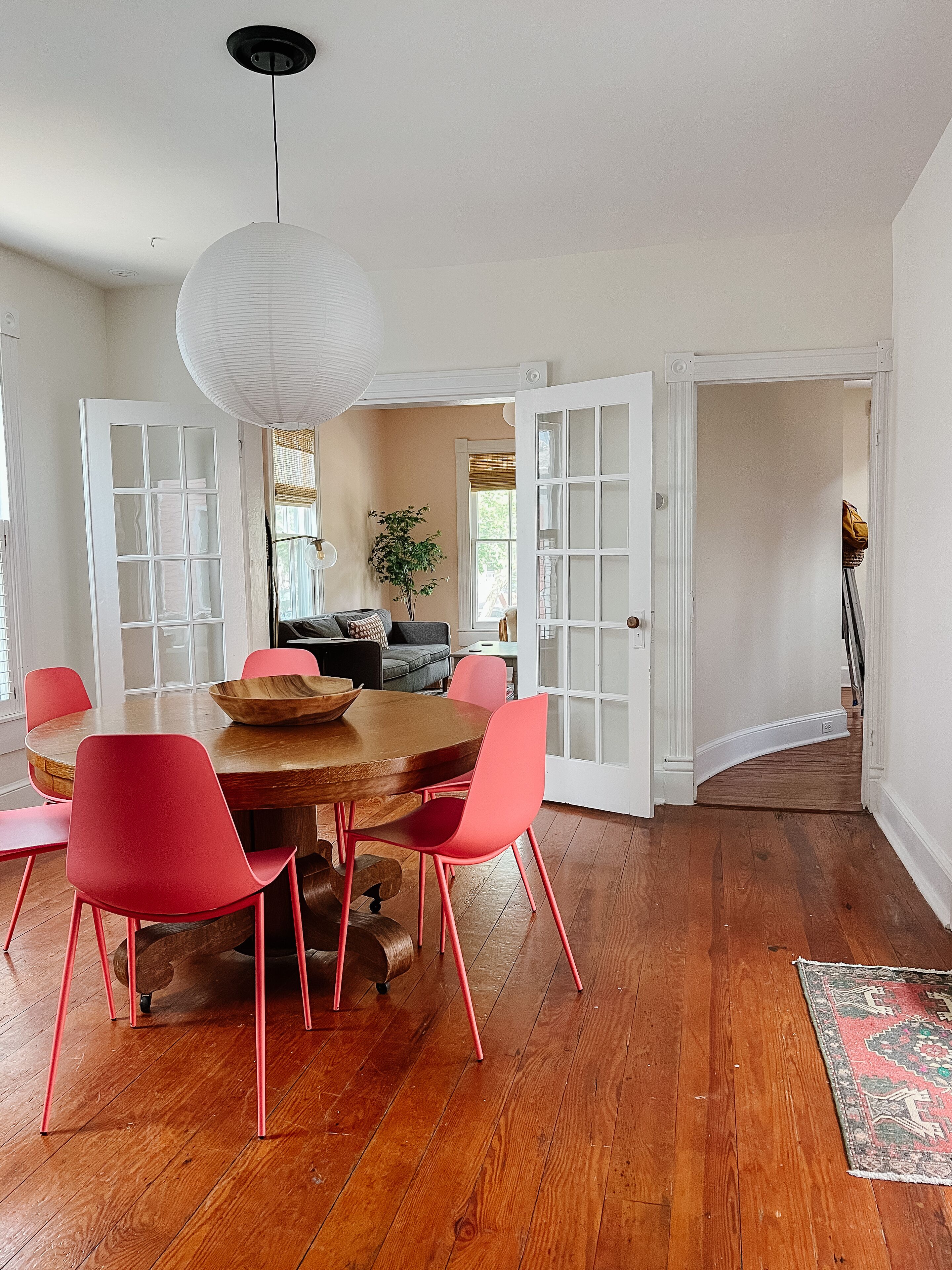 A dining area with a wooden table and red chairs, a white pendant light, and a wooden floor.