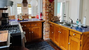 Een keuken met een gasfornuis, houten keukenkastjes, een accentmuur van baksteen en een groot raam.