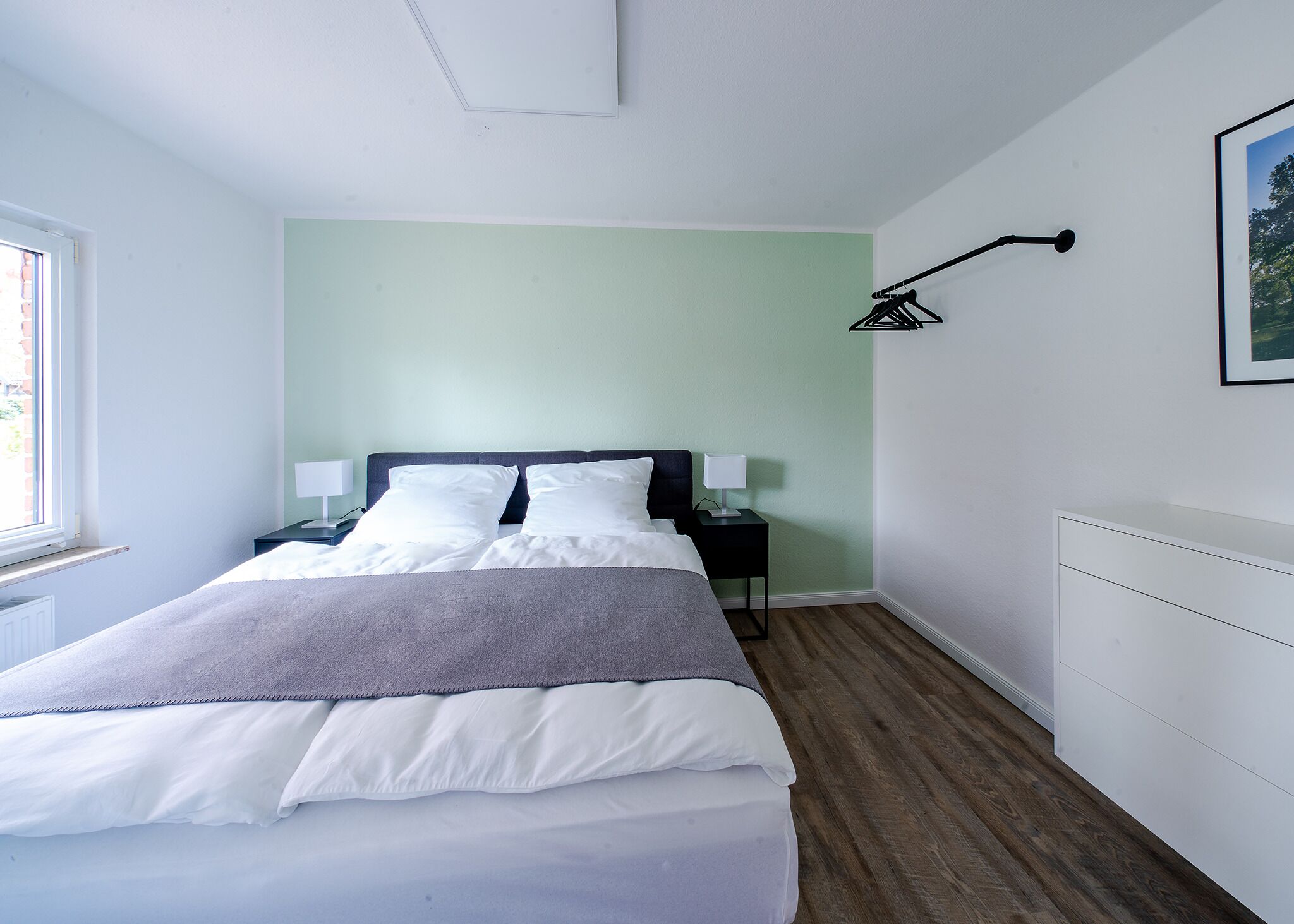 Un letto rifatto con lenzuola bianche, una coperta grigia e due comodini con lampade.