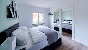 A modern bedroom with a large bed, a window, and a view of another room.