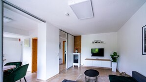 A modern living room with a sofa, a TV mounted on the wall, a fireplace, and a dining area with chairs.