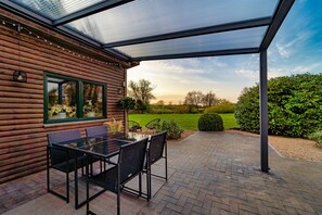 A wooden cabin with a glass patio, outdoor seating, and a view of the landscape. - Ferienhaus Direkt an der Wümme (Hellwege)