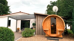 A modern house with a large wooden barrel structure, a satellite dish, and a well-maintained garden.