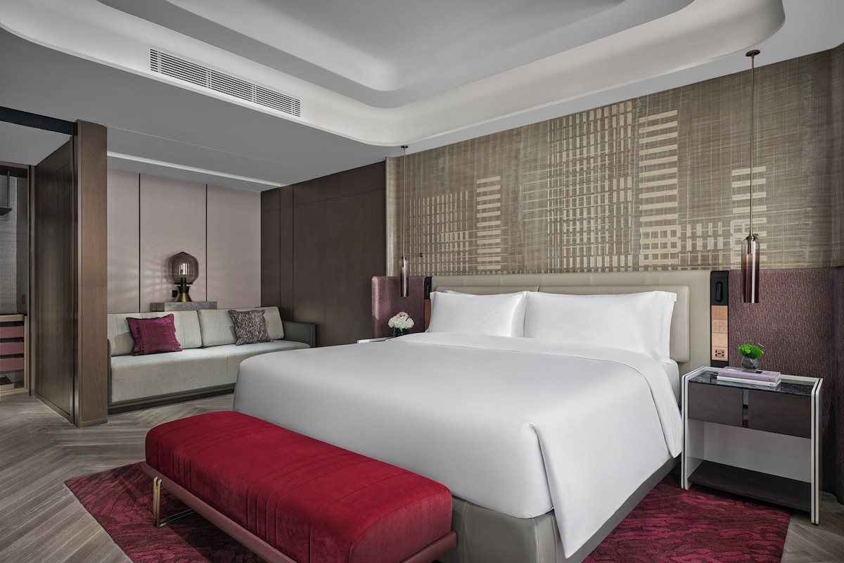 A modern hotel room with a large bed, a bench, a nightstand, and a patterned wall.