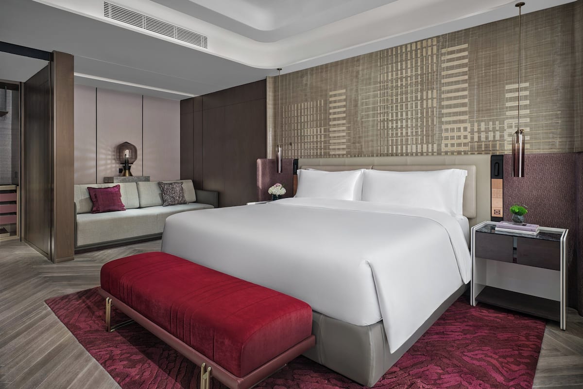 Una habitación de hotel moderna con una cama grande, un banco, una mesita de noche y un papel tapiz estampado.