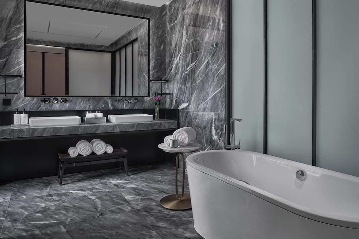 Un baño moderno con una bañera independiente, dos lavamanos, un mueble de tocador y un banco con toallas.