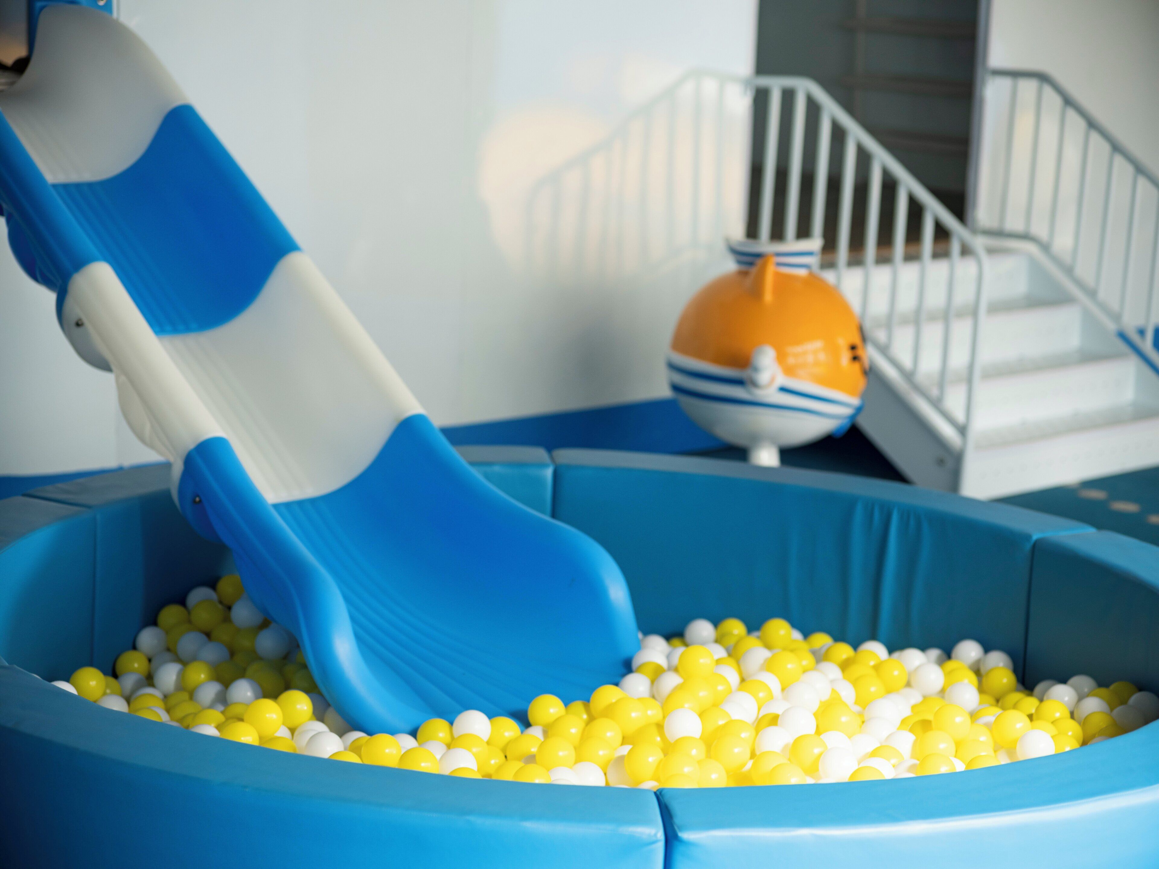 Zona de juegos con un tobogán azul y una piscina de pelotas llena de bolas amarillas y blancas.