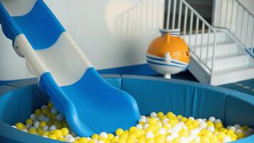 Zona de juegos con un tobogán azul y una piscina de pelotas llena de bolas amarillas y blancas.