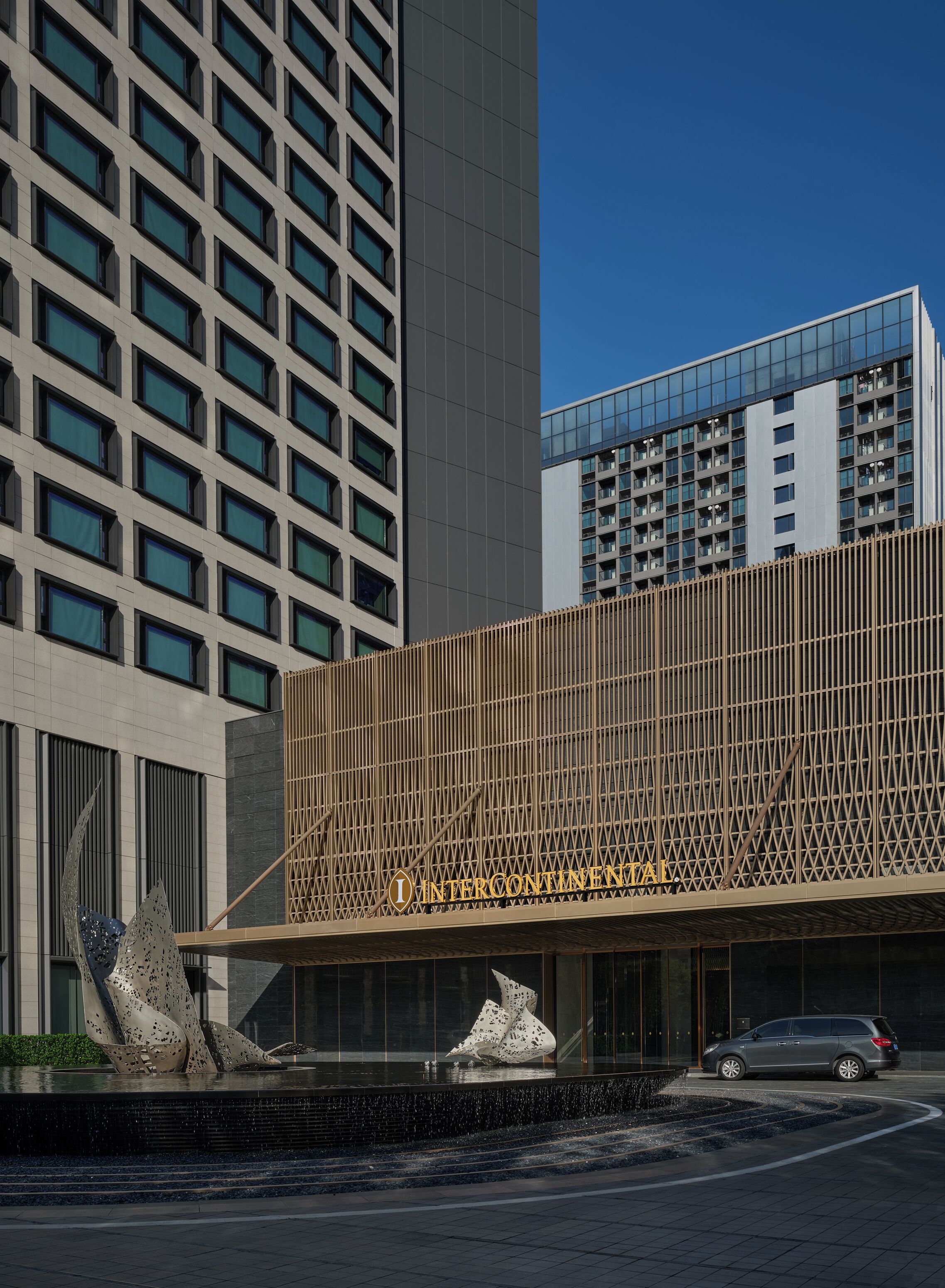 A modern building with a distinctive facade, a large sculpture in front, and a car parked nearby.